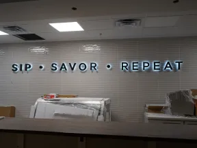 Illuminated wall sign reading Sip Savor Repeat in a modern interior with unpacked boxes and construction materials.