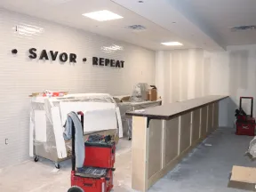 Under-construction restaurant interior with slogan Savor Repeat on tiled wall and bar counter being built.