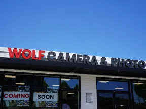 Storefront of Wolf Camera & Photo with a clear blue sky and Coming Soon signs in the windows.