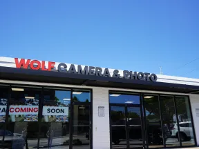 Storefront of Wolf Camera & Photo with signage and Coming Soon banners under a clear blue sky.