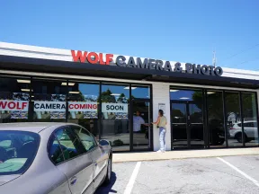 Wolf Camera & Photo store front with signs announcing the camera shop coming soon and people entering the store.