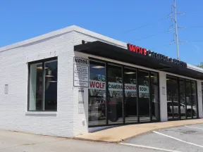 White brick storefront with glass windows displaying Wolf Camera coming soon signs under clear blue sky