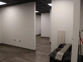 Empty office space with gray walls, wood-look flooring, and various building materials and tools inside.