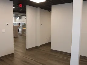 Empty modern office space with wood-look flooring, white walls, and a ceiling with black tiles and exit sign.