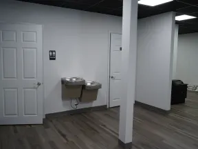 Interior of a modern indoor space with two white doors, dual water fountains, and wood-look flooring.