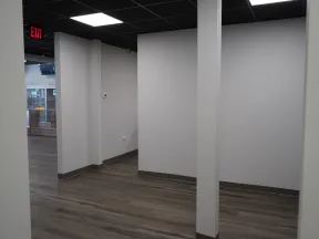 Empty office space with gray walls, wood flooring, and black tiled ceiling with exit sign.