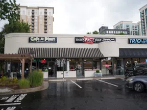 Storefronts of Cafe A Pharr, moreSPACEplace, and TRIO Shoe Service in an urban shopping plaza with parked cars.