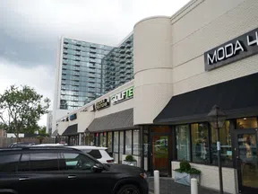 Modern retail strip with Moda House and other stores under cloudy sky and black SUV parked outside.