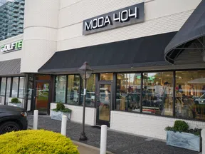 Moda 404 storefront with black awning on white brick building, adjacent to Golftes and Cookie Creations shops.