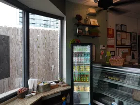 Interior of a cozy shop with a glass refrigerator stocked with beverages and snacks, and a counter with various items.