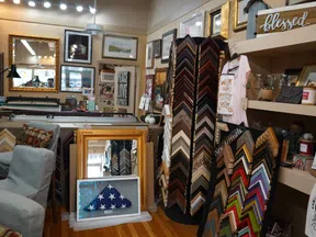 Interior of a frame shop showing various picture frames, mirrors, art prints, and decorative items on shelves.