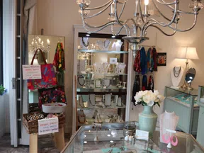Bright boutique interior with glass jewelry displays, colorful scarves, and decorative flowers in a vase.