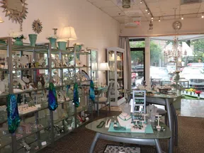 Bright jewelry store interior with glass display shelves, tables showcasing necklaces, rings, and decorative lamps.