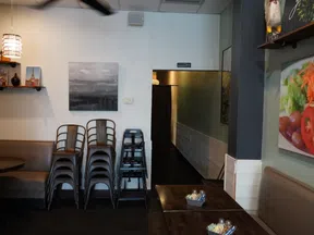 Cozy restaurant interior with stacked metal chairs, dark wooden tables, and vibrant food artwork on the walls.