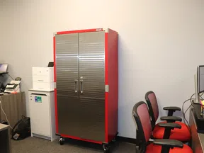 Red and silver metal storage cabinet in office room with chairs, desks, and computer monitors around it.