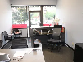 Modern office reception area with desk, chairs, laptop, paperwork, and large glass door letting in natural light.