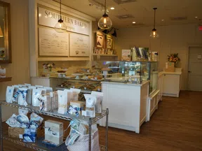 Cozy bakery interior with glass display cases of pies, wooden floors, hanging lights, and packaged goods on metal shelves
