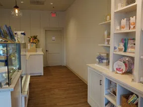 Interior view of a clean, modern bakery or cafe with wooden floor and white shelves displaying packaged goods.