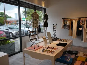 Boutique clothing store interior with mannequins, dresses, accessories, and large front windows showing parked cars.