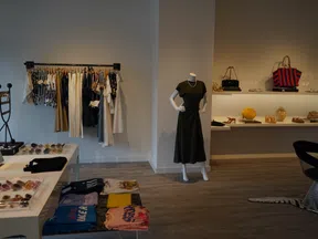 Modern boutique interior with clothing rack, mannequin in black dress, shelves with bags and accessories.