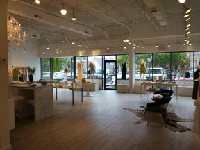 Spacious modern clothing store with mannequins, large windows, hardwood floors, and elegant lighting fixtures.