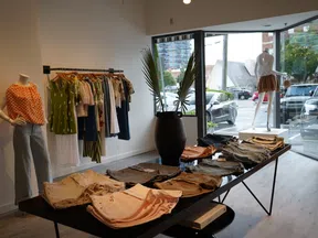 Modern boutique clothing store with casual wear displayed on table, rack, and mannequins by large windows.