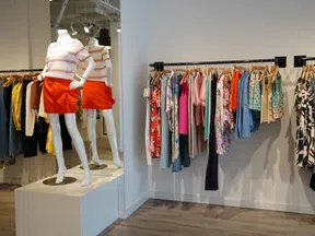 Bright clothing store interior with mannequins and colorful garments hanging on racks against white walls.