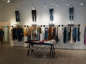 Modern clothing store interior with mannequins, hanging clothes, folded apparel, and seating area under soft lighting