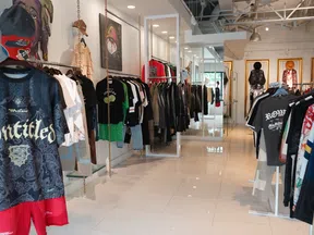 Modern clothing store interior with hanging shirts, jackets, and streetwear displayed on white tile floor.