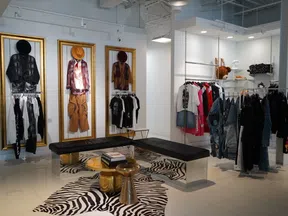Modern boutique interior with stylish clothing displays, framed outfits, black seating, and zebra print rug.