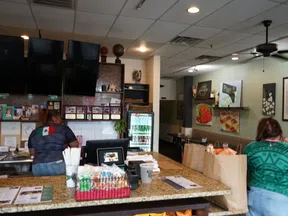 Interior of a casual restaurant with two workers behind the counter and takeout bags on the table.