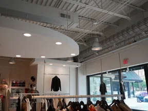 Modern clothing store interior with hanging racks displaying jackets and shirts under industrial ceiling lighting.