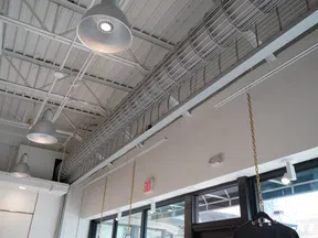 Industrial ceiling with hanging lamps, metal wiring trays, and large windows in a modern commercial space.
