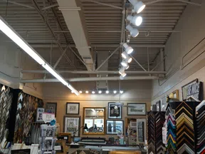 Interior of a frame shop with various picture frames, artwork, mirrors, and bright overhead lighting