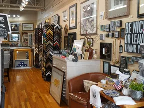 Interior of a custom framing and gift shop with artwork, picture frames, and decorative signs on display.
