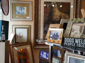 Interior display featuring framed photos, art prints, wine bottles, and decorative signs on shelves and walls.