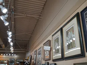 Gallery wall with framed artwork and photos illuminated by ceiling track lighting in an art sale exhibition space.