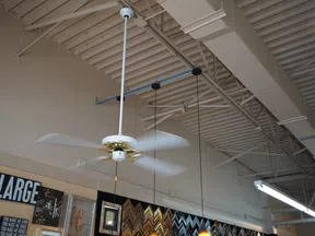 White and gold ceiling fan spinning in industrial space with pendant lights and framed art on wall below