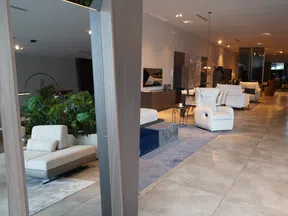 Modern living room interior with white sofas, armchairs, plants, and warm lighting on tiled floor.
