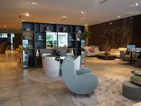 Modern open living room with diverse seating, decorative shelves, marble wall, and neutral tiled flooring