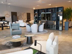 Modern living room with white and gray furniture, round tables, large bookshelf, and decorative vases in spacious interior.