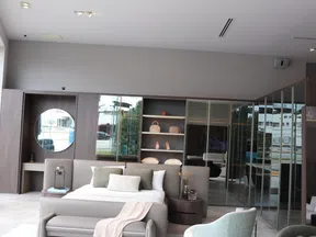 Modern bedroom interior with a large bed, soft pillows, a bench, and mirrored wardrobe doors in neutral tones.