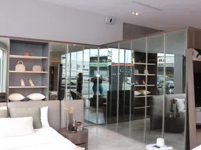 Modern bedroom with mirrored closet doors, shelves with shoes and pillows, and a bed with cushions.