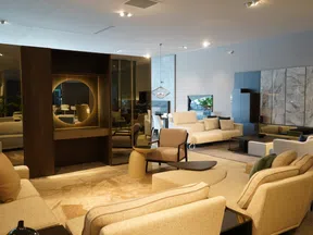 Spacious modern living room with beige sofas, armchairs, circular mirror, and warm ambient lighting.