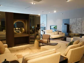 Modern living room with beige sofas, armchairs, wooden accents, glass table, and decorative round mirror on wall