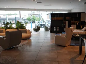 Modern furniture showroom with sofas, armchairs, a bed, and large windows overlooking a street with stores.