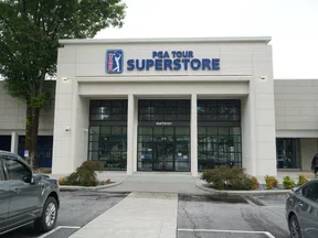 Exterior view of PGA TOUR Superstore with parked cars and trees under a cloudy sky.
