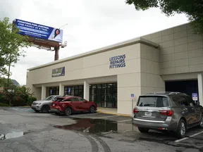 Storefront with signs for lessons, repairs, and fittings beside a parking lot with three cars and a justice billboard above.