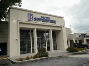 Exterior view of PGA Tour Superstore with large glass doors and adjacent Men's Wearhouse store in a shopping center