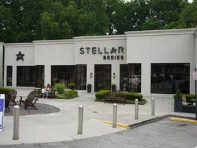 Exterior view of Stellar Bodies fitness studio with outdoor benches, greenery, and parking area in front.